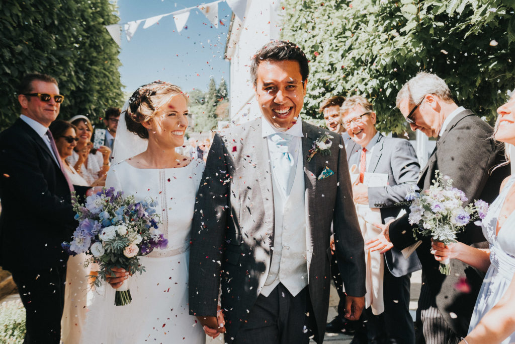 bride and groom walk through confetti smiling kent wedding photographer