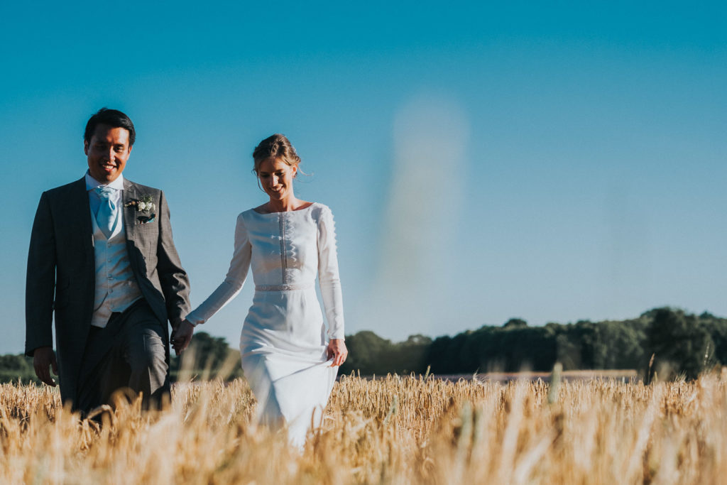 kent wedding photographer bride and groom walking through wheat field in summer blue sky